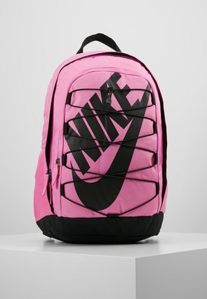 Růžový nylonový batoh s velkým černým logem Nike, nastavitelnými popruhy a elastickým šňůrováním na přední straně. Černý spodní základnu.