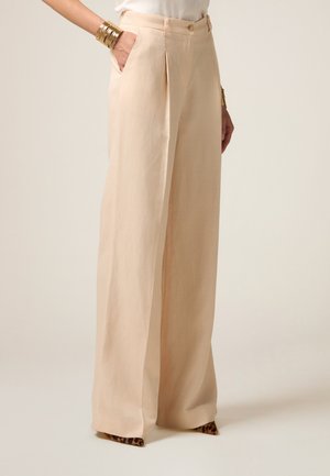 Pantalones de pierna ancha beige con una textura suave, que presentan pliegues delanteros y bolsillos laterales, rematados con un cierre de botón y acentos de estampado animal en el dobladillo.
