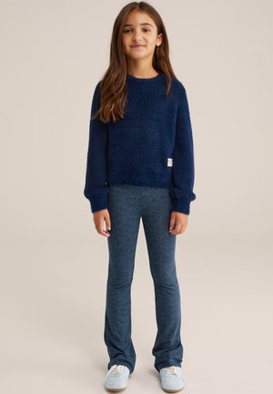 Donkerblauwe fluffy trui met lange mouwen, gecombineerd met gestreepte flared leggings met een golvend ontwerp en lichtblauwe sneakers.