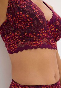 Bralette in pizzo di un ricco color prugna con accenti arancioni. Presenta un bordo a scallop e un motivo floreale. La texture leggera e morbida aumenta il comfort.
