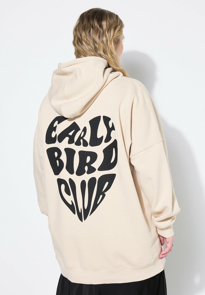 Sudadera beige con un gran gráfico negro en forma de corazón que presenta el texto "EARLY BIRD CLUB" en una tipografía audaz y divertida. Tela suave, corte relajado.
