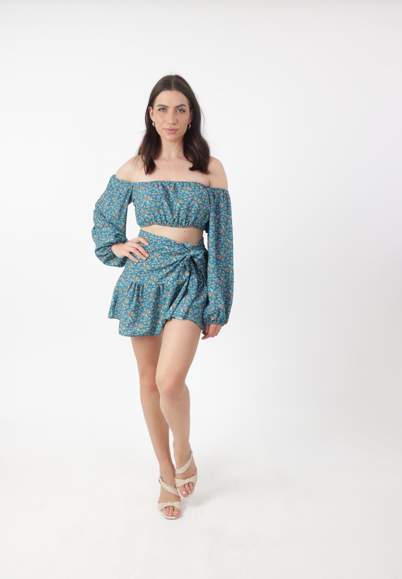Set di due pezzi composto da un crop top off-the-shoulder e una mini gonna, realizzato in tessuto blu con piccoli motivi floreali. Leggero e con una texture unica.