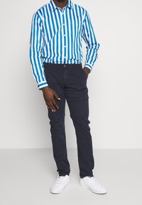Blauw-wit gestreepte overhemd met knopen en een borstzak, gecombineerd met donkerblauwe broek en witte sneakers. Zachtheid van de stof, op maat gemaakte pasvorm.