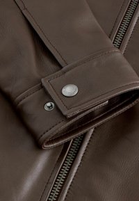 Barna bőrkabát részlet, cipzáros nyitással, patentos záródással és eltérő varrással az ujjak végén.