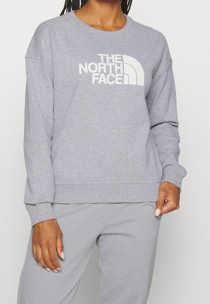 Sweat-shirt gris en polaire, arborant un logo blanc "THE NORTH FACE" sur la poitrine, avec un col rond classique et des poignets côtelés.