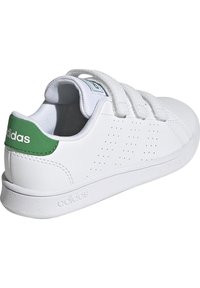 Zapatillas blancas con un acabado de cuero liso, tres correas de velcro y un acento verde en el talón que presenta el logo de Adidas.