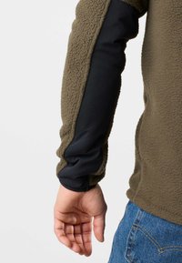 Fleecejacke mit einem olivgrünen Körper und schwarzen, dehnbaren Ärmeln. Hat eine strukturierten Oberfläche und ein tailliertes Design mit einem glatten Bündchen.