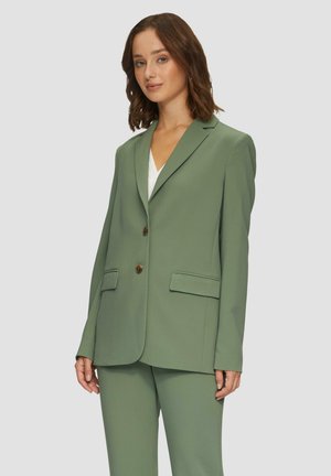 Blazer vert ajusté avec deux boutons, revers crantés et deux poches avant. Associé à un pantalon vert assorti, texture de tissu lisse.
