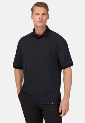 Polo negro de manga corta con cuello, con tejido texturizado y una etiqueta de logo en el dobladillo inferior, combinado con pantalones oscuros.