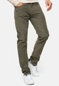 Olivengrønne fløjlbusker med slim fit, der har sidelommer og en tekstureret overflade, parret med hvide sneakers.
