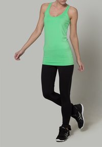 Zelený sportovní top s těsným střihem, v kombinaci s černými legínami se bočními akcenty. Model má na sobě černé tenisky.
