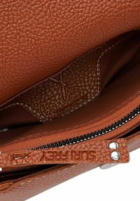 Innenseite einer handgefertigten tannfarbenen Lederhandtasche mit strukturiertem Oberflächenmaterial, ausgestattet mit einem Reißverschluss und einer geprägten Markenkennzeichnung am Reißverschlusszieher.