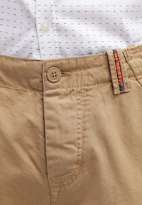 Shorts en khaki beige avec un tissu texturé, dotés d'une fermeture à bouton et d'une étiquette portant le nom de la marque "Superdry" en orange.