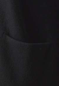 Svart ulltyg med en mjuk textur, som har en framficka. Bilden framhäver textilets släta yta och tjocklek.