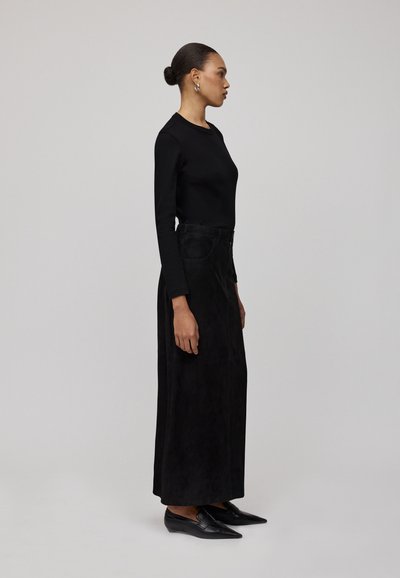 Schwarzes Langarmoberteil, schwarze Wildleder-Maxirock und schwarze spitze Ballerinas. Einfaches Design mit einer taillierten Silhouette und minimalen Verzierungen.