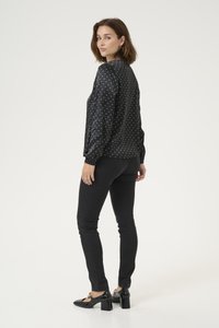 Blusa nera a maniche lunghe con pois bianchi, dal fit rilassato e con polsini arricciati. Abbinata a jeans skinny neri e scarpe a blocco in pelle lucida.