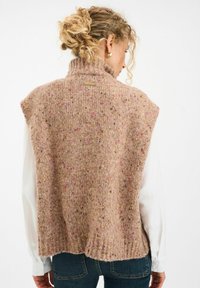 Kootud vest heledas pruunis värvitoonis, millel on värvilised täpid, kõrge kaelus ja soonikserv. Omab vabalt langevat lõiget ja lühikesi varrukaid.