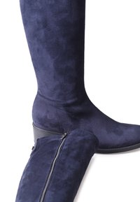 Bottes montantes en daim bleu marine avec un design élégant, dotées d'une fermeture éclair discrète et d'une semelle en caoutchouc plate. Surface texturée mise en valeur.