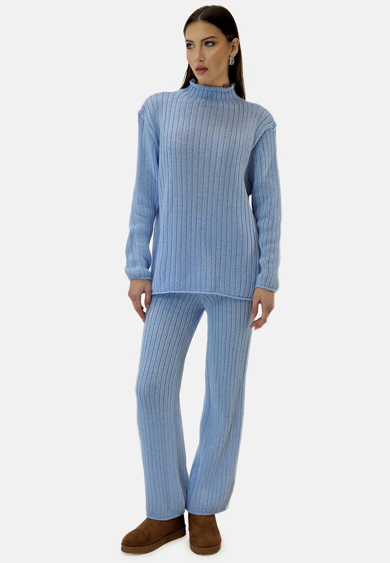 Jasnoniebieski, prążkowany sweter z wysokim kołnierzem w komplecie z dopasowanymi prążkowanymi spodniami. Modelka nosi brązowe botki. Miękka tekstura, luźny krój.