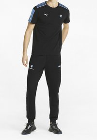 Sort atletisk T-shirt med korte ærmer og blå accenter, BMW-logo på brystet; matchende sorte bukser med BMW-logoer, elastiske manchetter og figursyet design.