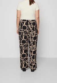Pantalones de pierna ancha en negro con un patrón geométrico en beige claro. Fabricados con un tejido suave, tienen un ajuste holgado y una cinturilla elástica.