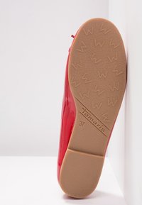 Sula av en röd platåsko med ljusbrun gummisula som har "Tamaris"-logotyp och präglad storlek nummer 37, fotograferad mot vit bakgrund.