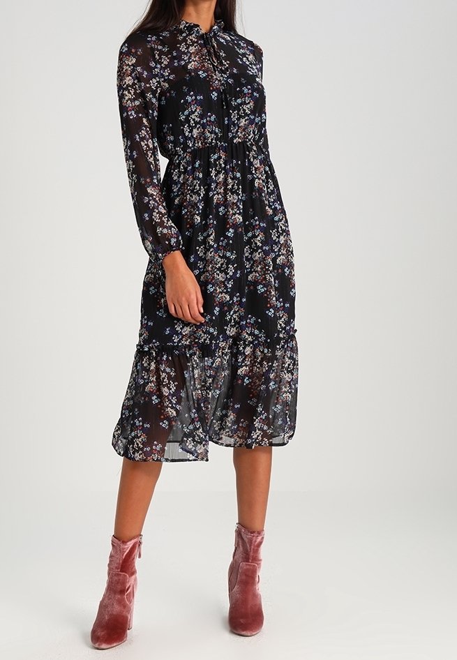 Mustaa kukkamekkoa, joka on valmistettu läpikuultavasta kankaasta, jossa on pitkät hihat, solmittava kaulus ja kerroksellinen helma. Yhdistetty vaaleanpunaisiin samettisiin nilkkabootseihin.