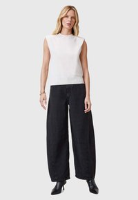 Witte mouwloze top met geribbelde onderrand en schouderdetail, gecombineerd met wijde zwarte broek met een gladde textuur en subtiele stiksels.