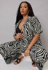 Svartvit zebra-randig outfit med kortärmad skjorta med knappar och vida byxor, matchat med svarta sandaler med en dekorativ rem.