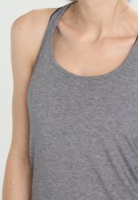 Grå sportig linne tillverkat av mjukt, strukturerat tyg. Har en rundad halsringning och racerback-design, med en lätt drapering vid midjan.