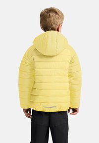 Chaqueta acolchada amarilla con capucha, que presenta secciones acolchadas horizontales y un detalle reflectante en el dobladillo; diseño ligero y moderno.
