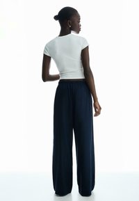 Bela, prilegajoča majica s kratkimi rokavi v kombinaciji z ohlapnimi temno modrimi hlačami. Mehka tkanina; majica ima kratke rokave, hlače pa so opremljene z elastiko v pasu.