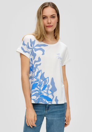 T-shirt blanc avec un motif de feuilles abstraites bleues, à manches courtes, col rond et coupe décontractée, associé à un jean bleu.