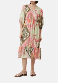 Sukienka z dekoltem w kształcie litery V, z krótkimi bufkami, w jasnym zielonym kolorze z kwiatowym wzorem w odcieniach różu, pomarańczu i brązu. Posiada warstwowy dół oraz pasujący pasek.