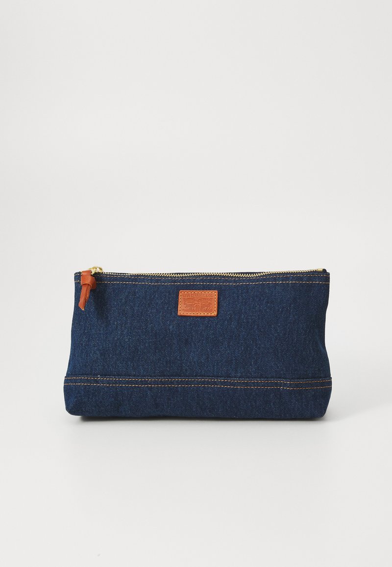 Denim-pose med en lærlabel i tan, gullglidelås og oransje søm. Rektangulær form, egnet for oppbevaring eller organisering.