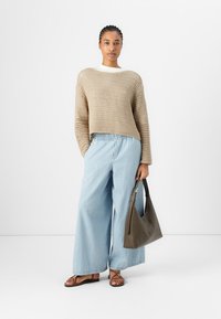 Beige gestrickter Crop-Pullover, hellblaue weit geschnittene Jeans, braune Sandalen und eine dunkelgrüne Tasche. Hat ein offenes Gewebe und eine entspannte Passform.