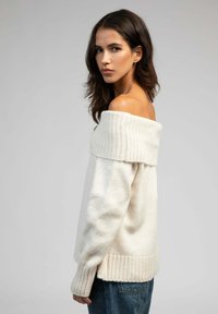 Pull en maille crème décolleté, avec des poignets et un ourlet côtelés. Texture lisse, coupe décontractée et fentes latérales pour un confort optimal.