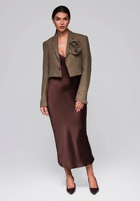 Brun satäng midi-klänning i kombination med en kort, texturerad brun jacka med blommor som utsmyckning. Spetiga, mörka klackar fulländar stilen.