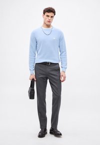 Világoskék mintás pulóver, szürke szabott nadrág, fekete bőrcipő és fekete válltáska. Ezüst lánc medál díszítés.