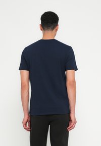 Jūras zilas īsām piedurknēm t-krekls ar apaļu kakla izgriezumu, izgatavots no gludas kokvilnas auduma. Vienkāršs dizains, neredzami logotipi vai raksti.