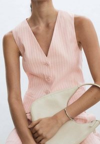 Różowa bluzka w prążki bez rękawów z głębokim dekoltem w serek i trzema guzikami, zestawiona z kremową torebką trzymaną na ramieniu.