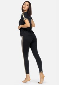 Czarna sportowa bluzka i legginsy z złotymi akcentami na rękawach i bocznych szwach. Gładki, dopasowany fason o miękkiej fakturze. Gołe stopy.