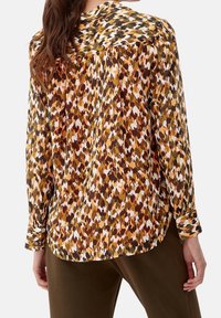 Camicia a maniche lunghe con colletto, in un motivo astratto multicolore, con sfumature di marrone, arancione e crema. Tessuto morbido, vestibilità comoda.