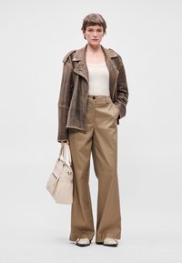 Brūnas ādas motokrosa jaka pāri beigu krāsas bez piedurknēm, kombinēta ar tan krāsas platajām biksēm un krēmkrāsas apaviem. Tur neitrālu krāsas rokassomu.