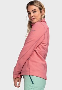 Hellrosa Fleecejacke mit hohem Kragen, Reißverschlusstaschen und kontrastierenden Nähten. Besitzt ein Logo auf der Schulter und hat eine lockere Passform.