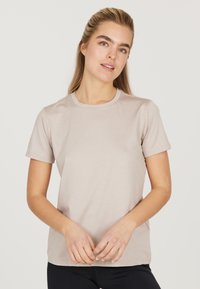 Ljusbeige t-shirt med kort ärm, klassisk rundhalsdesign, mjukt bomullsmaterial, minimal branding på bröstet, slät textur.