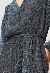 Robe portefeuille métallique noire et bleue avec une texture côtelée horizontale, taille cintrée et manches larges. Dotée d'une ceinture nouée assortie en tissu.