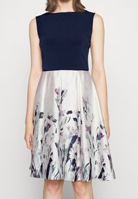 Šaty bez rukávů s námořnickým topem a saténovou sukní s květinovým vzorem v jemných odstínech fialové, zelené a černé, se rozšířeným siluetem.