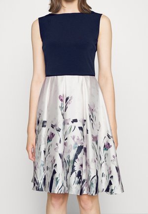Mouwloze jurk met een marineblauw lijfje en een satijnen rok met bloemenpatroon in zachte tinten van paars, groen en zwart, met een flared silhouet.