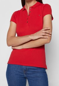 Camisa polo roja con cuello, tapeta de cinco botones y mangas cortas, hecha de algodón, con un pequeño logotipo en el lado izquierdo del pecho.